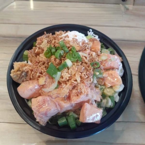 A poke bowl with salmon, rice, fried onions, and green onions in a black bowl.