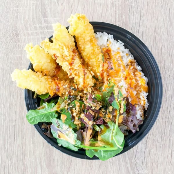 Top-down view of a black bowl with tempura shrimp, white rice, and a green salad.